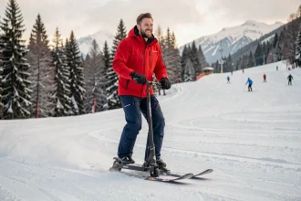 Adulte en veste rouge faisant de la patinette ski sur une piste damée des Alpes françaises
