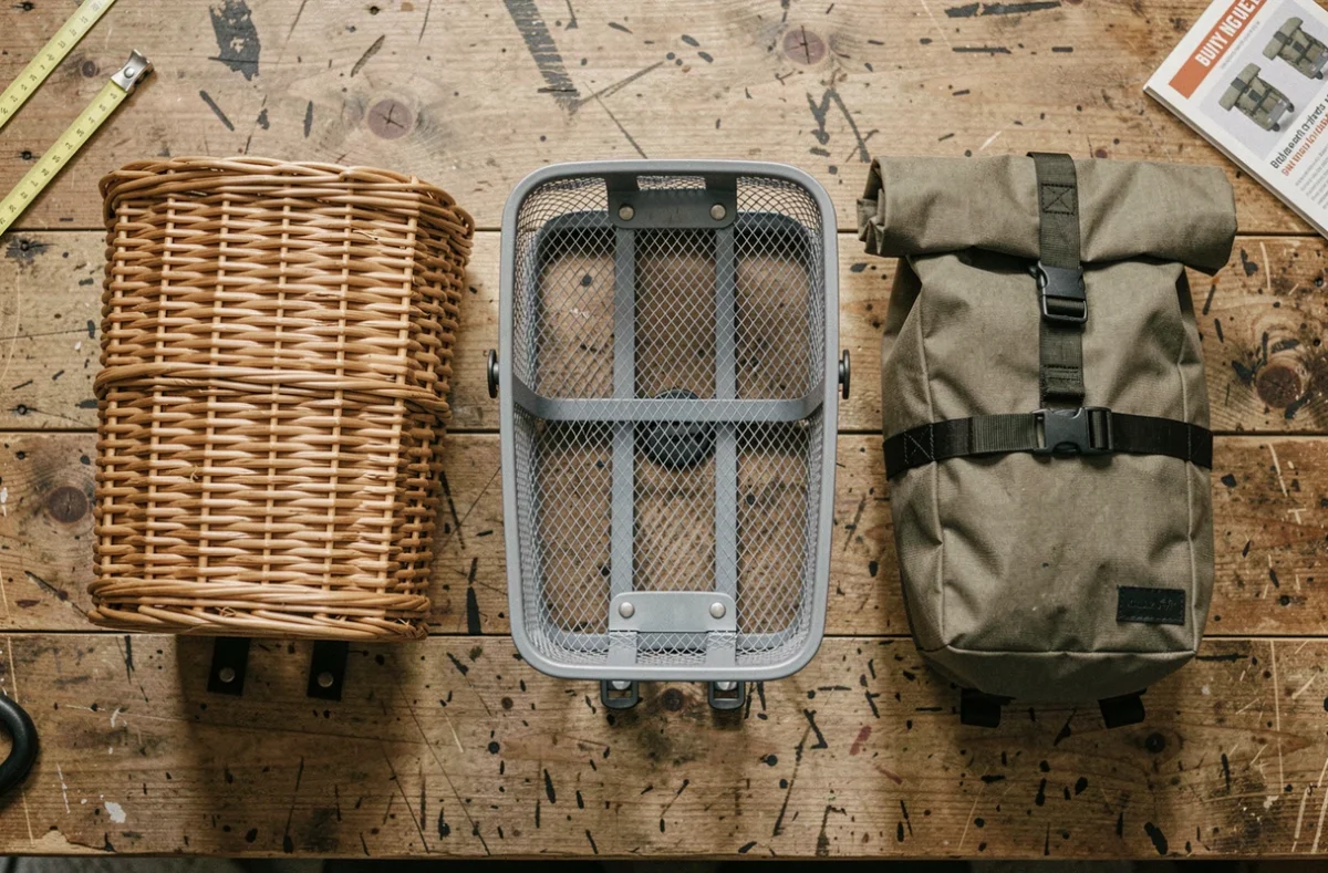 Comparaison de trois types de paniers extérieurs pour vélo posés sur une table en bois avec leur système d'accroche