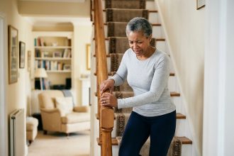 Femme d'âge mûr tenant la rampe d'escalier avec douleur au genou en descendant les marches chez elle